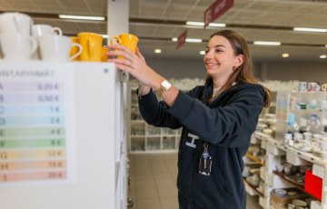 Nainen lajittelee kahvikuppeja hyllyyn.