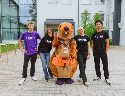 Kuva jossa nuoret seisovat rivissä hymyillen, yhdessä Hyrian Majava maskotin kanssa.